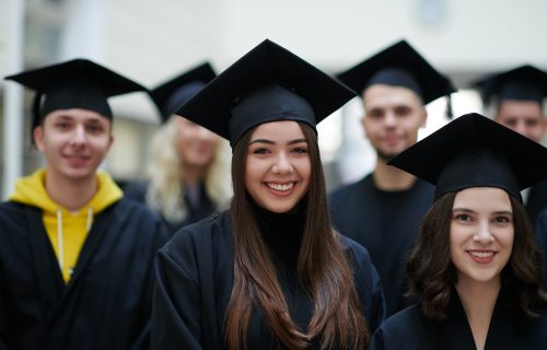 education, graduation and people concept - group of happy international students in mortar boards and bachelor gowns with diplomas